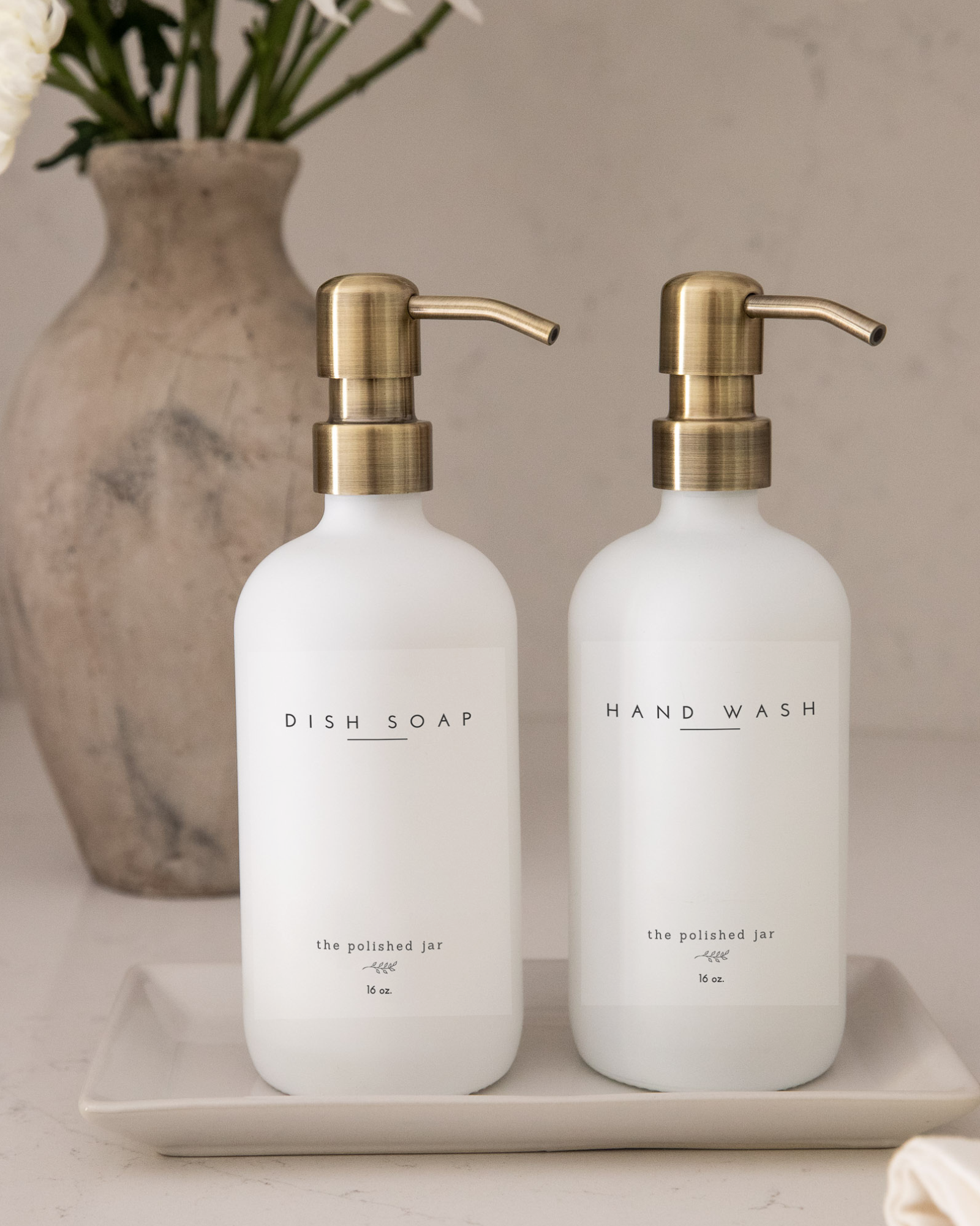 Two white bottles with gold pumps labeled 'Dish Soap' and 'Hand Wash' on a neutral background.