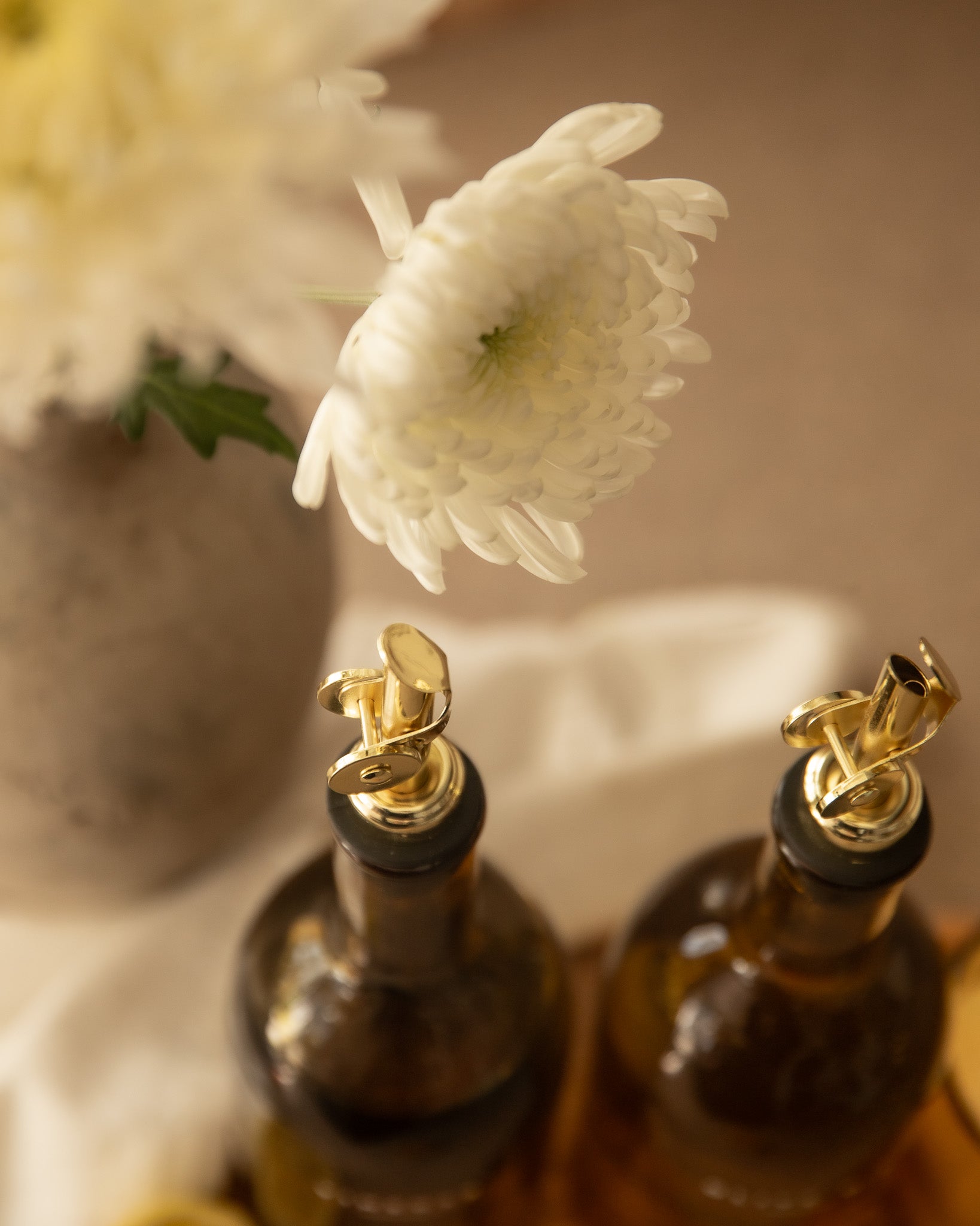 Two bottles with gold bottle pourers on a blurred background of flowers