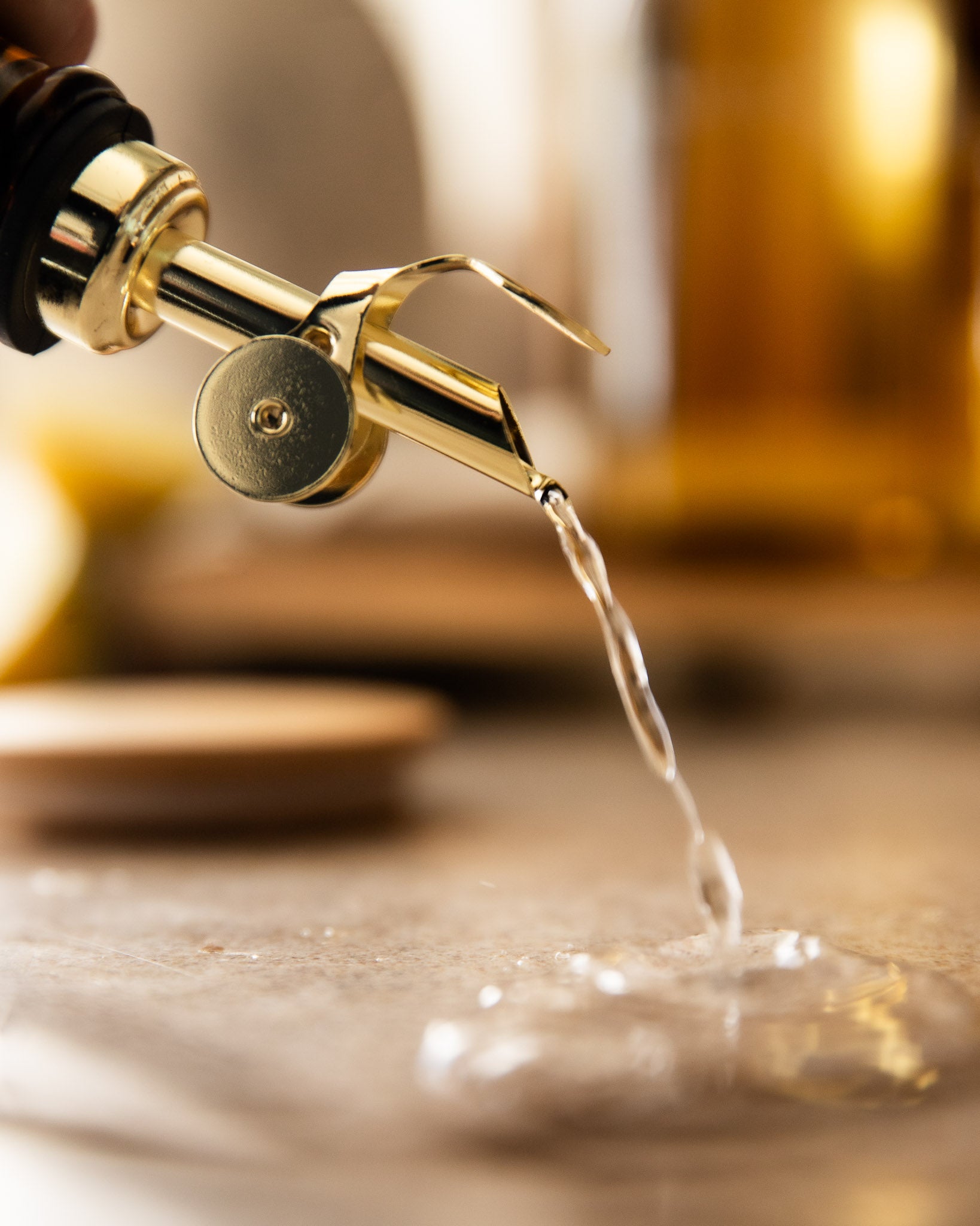 Gold Pourer pouring water onto a wooden surface with a blurred background