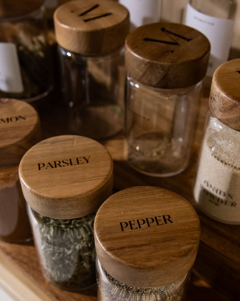 Collection of spice jars with monogrammed lids on a wooden shelf.