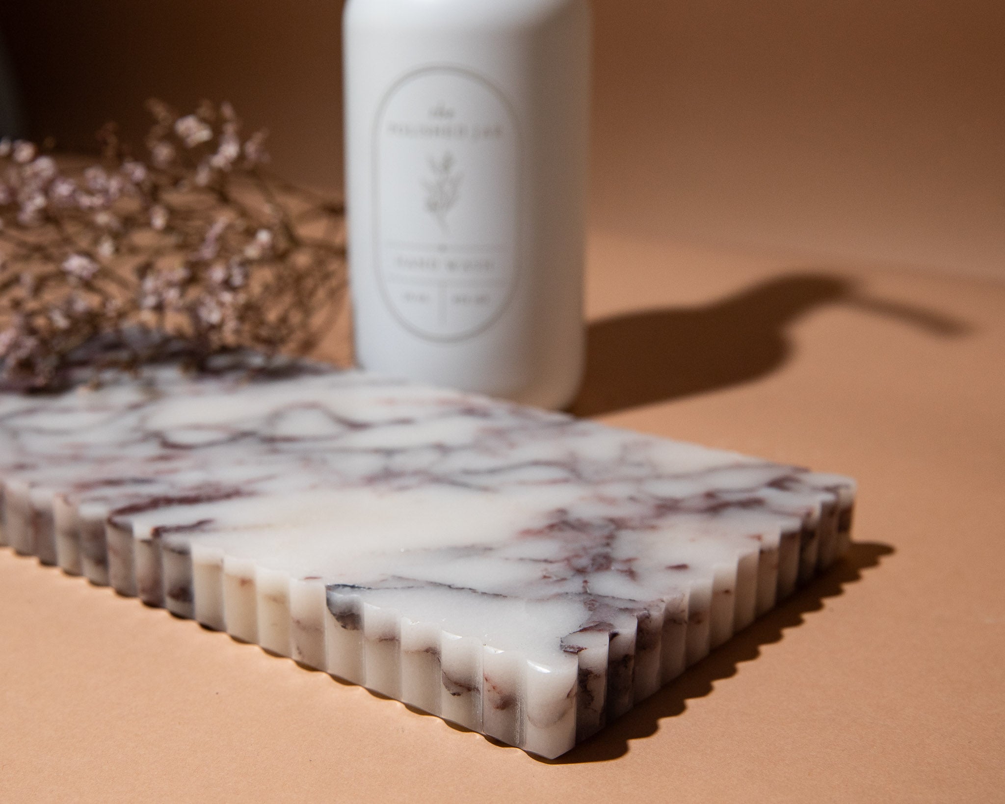 Marble-patterned cutting board with a white bottle on a beige surface