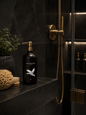Black shampoo bottle with a gold pump on a dark bathroom shelf.
