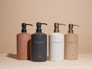Four concrete bottles of shampoo, dish soap, and hand wash on a beige background