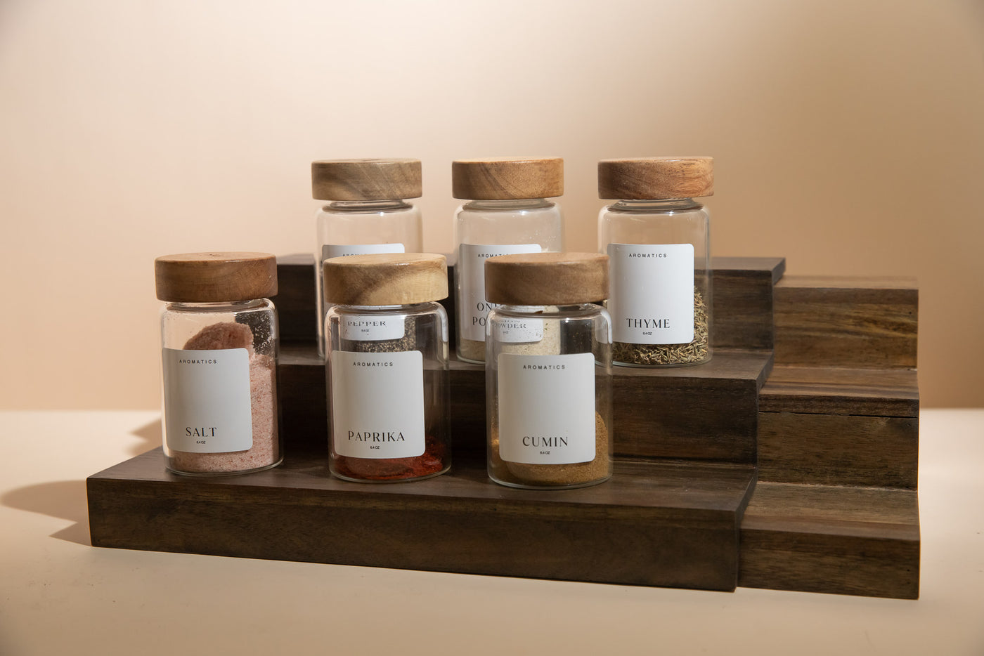 Set of spice jars with wooden lids on a wooden stand against a beige background