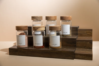 Set of spice jars with wooden lids on a wooden stand against a beige background