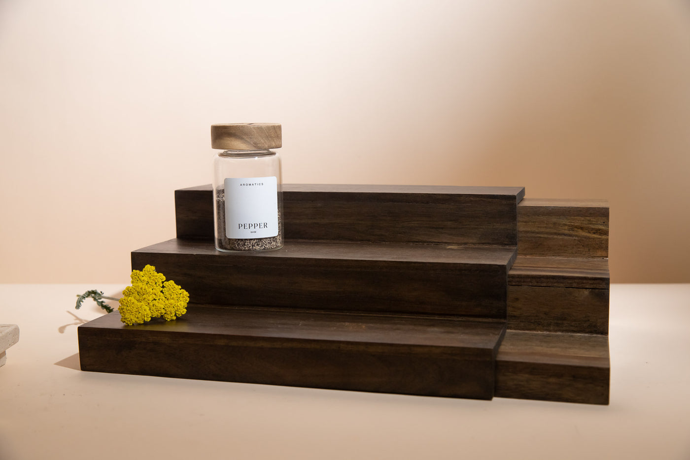 Wooden tray with a jar labeled 'Pepper' and yellow flowers on a beige background