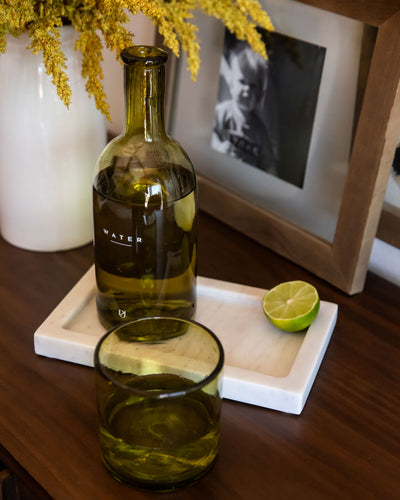 Green glass bottle labeled 'WATER' on a wooden surface with a lime and photo frame in the background.