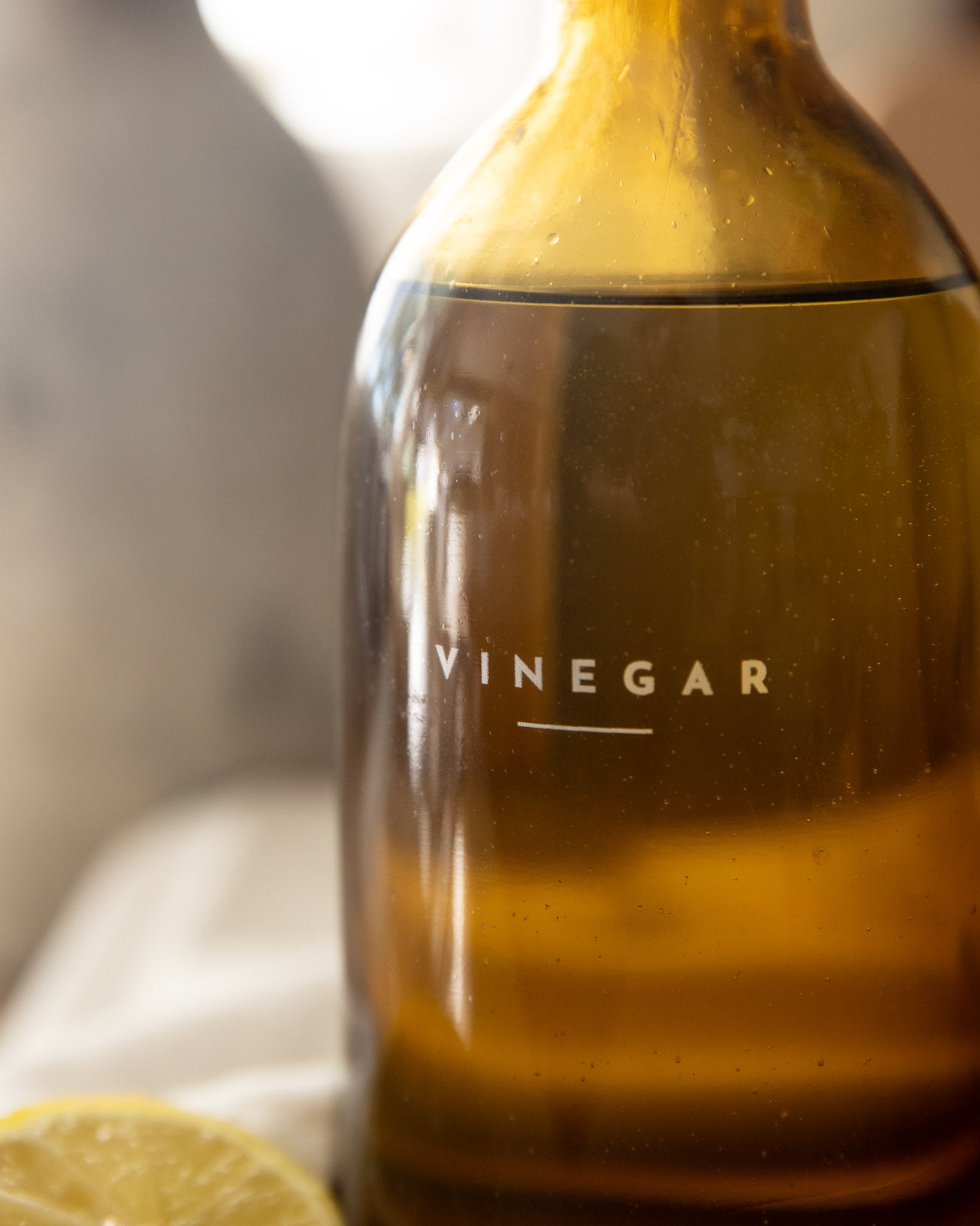 Bottle of vinegar with a lemon in the foreground on a blurred background