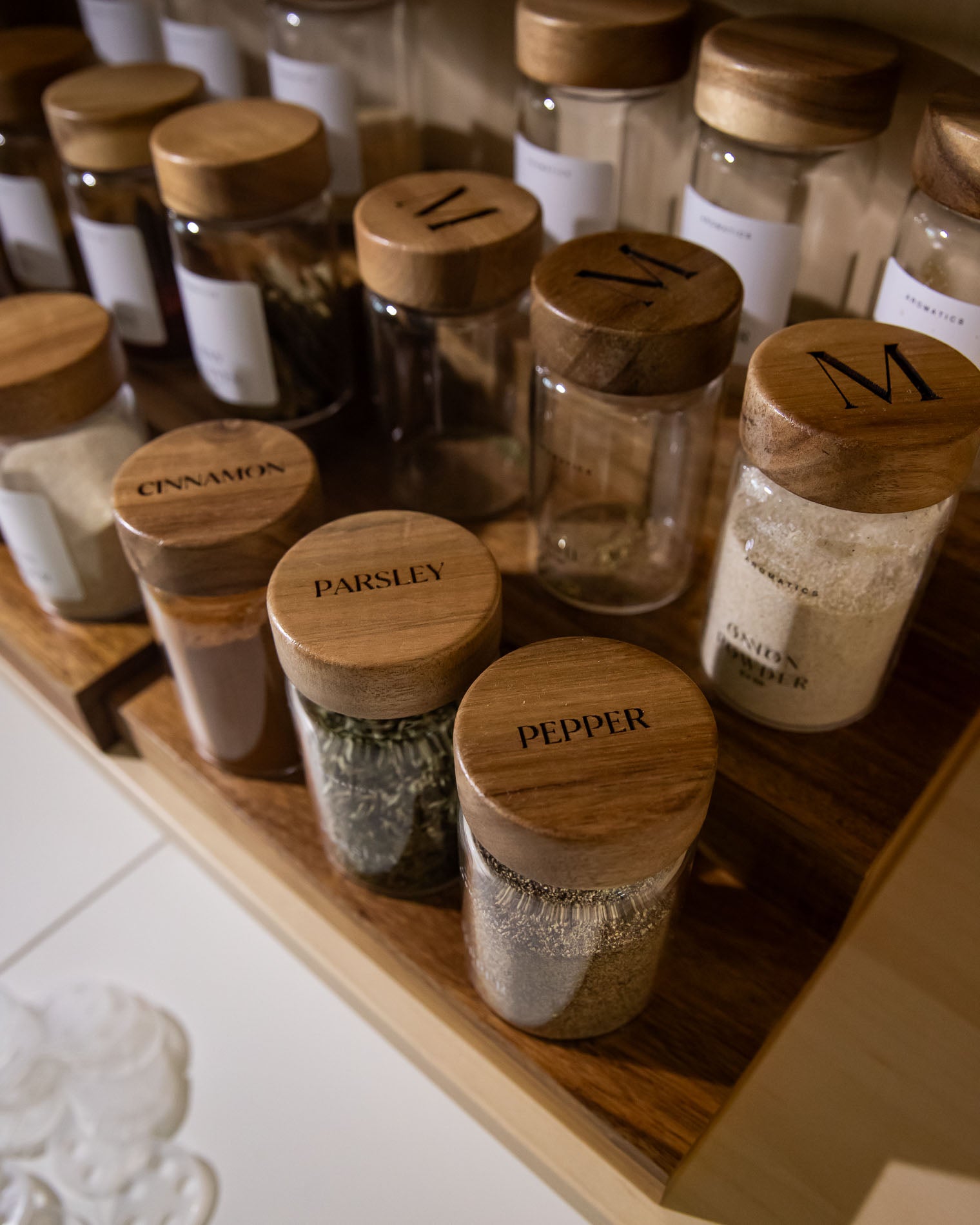 Collection of spice jars with monogrammed lids on a wooden shelf.
