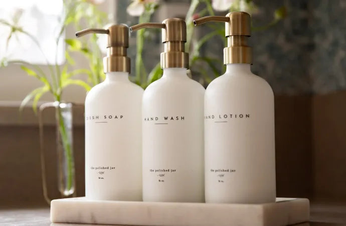 Three white spa soap dispenser bottles with gold pumps on a marble tray.