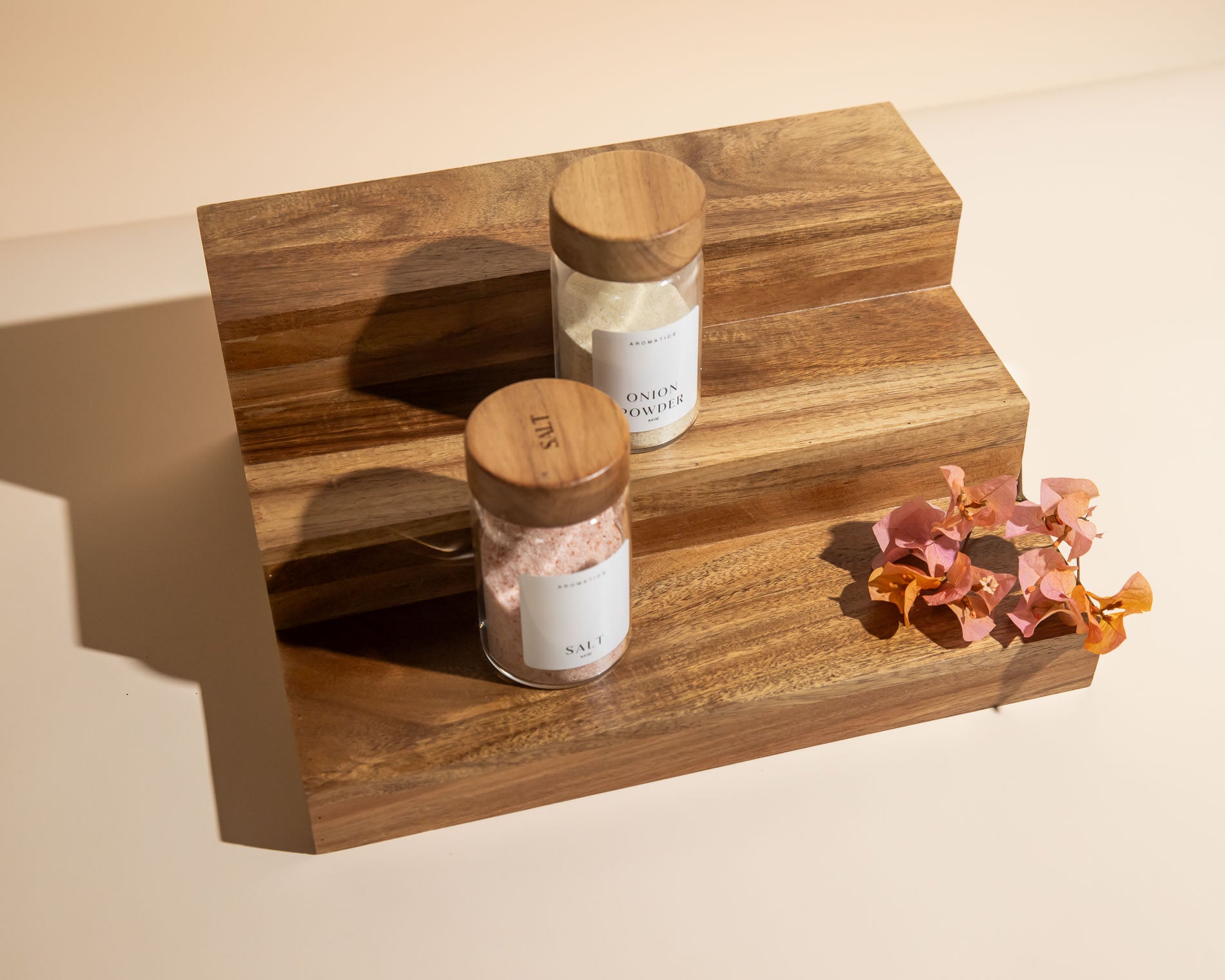 Acacia wooden spice rack with jars and decorative flowers on a beige background