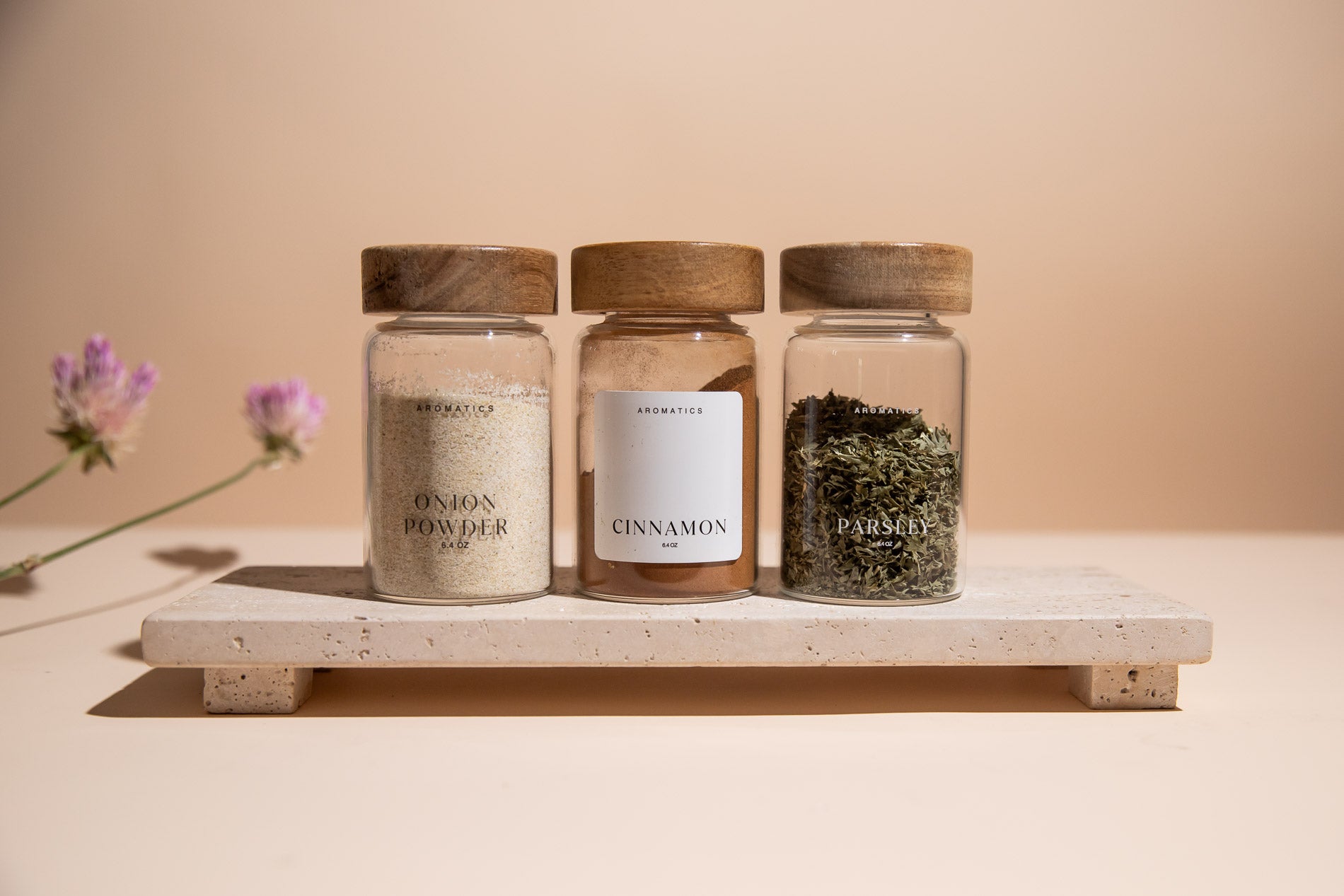 Three glass jars labeled 'Onion Powder', 'Cinnamon', and 'Herbs' on a wooden stand with a blurred background.